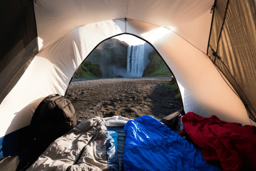 Sleeping bags in an open tent in the countryside next to a waterfall. Source: https://www.pexels.com/cs-cz/foto/svetly-lehky-krajina-priroda-2412023/