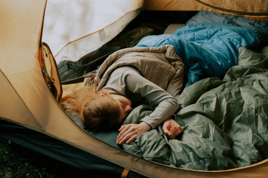 A woman sleeping in a sleeping bag in an open tent. Source: https://www.pexels.com/cs-cz/foto/osoba-zena-kempovani-spani-5994748/