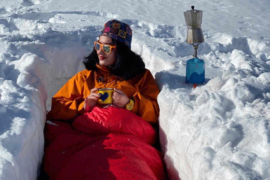 A woman with a mug tin sitting in a trench in a winter sleeping bag. Source: https://www.pexels.com/cs-cz/foto/ryma-studeny-snih-zena-10284511/