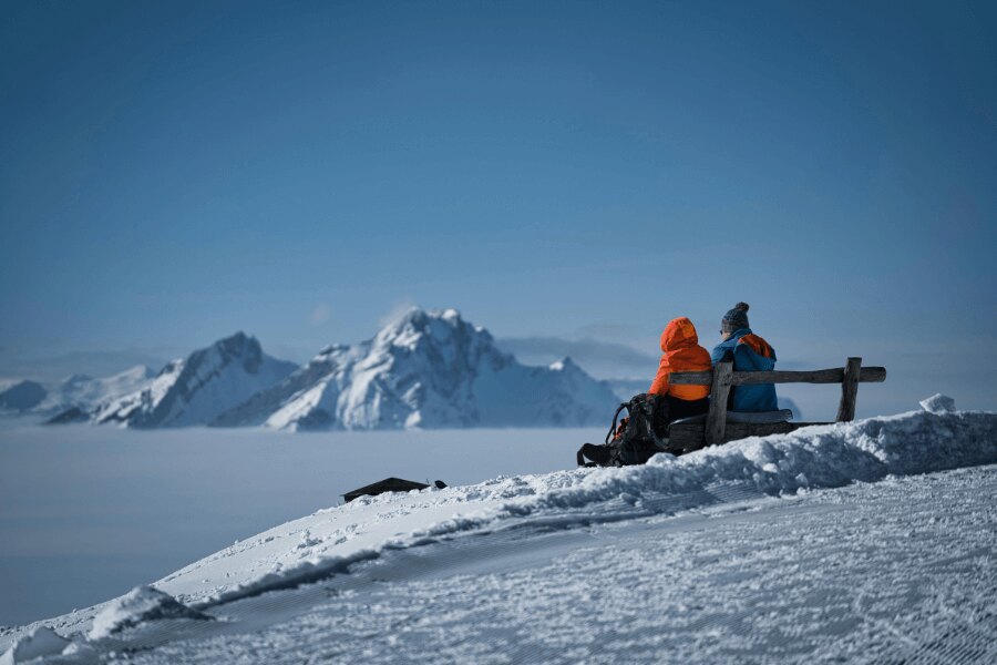 People sitting on a bench in the middle of snowy mountains. Source: https://www.pexels.com/cs-cz/foto/ryma-studeny-ledovec-snih-28211315/