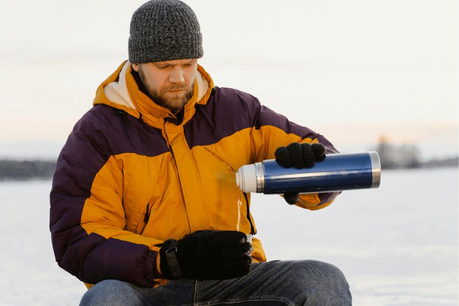 A man on ice drinking from a thermos. Source: https://www.pexels.com/cs-cz/foto/muz-sklenice-sklo-liti-6831055/