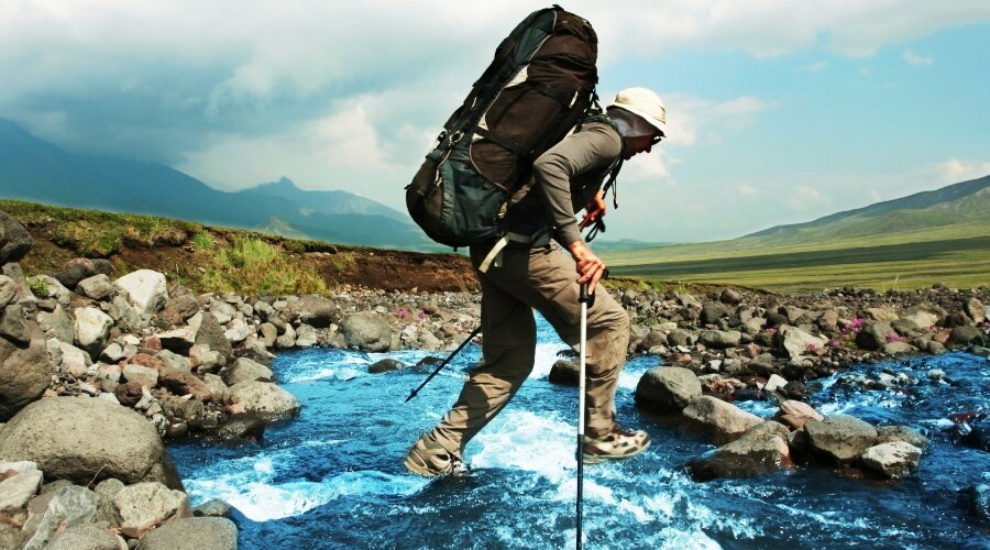 The man with sticks and a backpack crosses the river