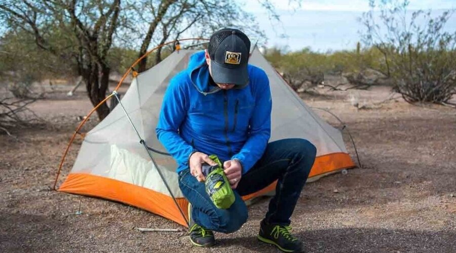 A man unpacking a mat in front of a tent