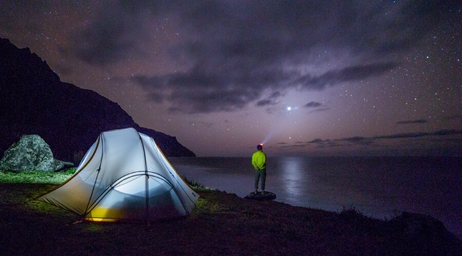 A man with a headlamp looking far at the sea