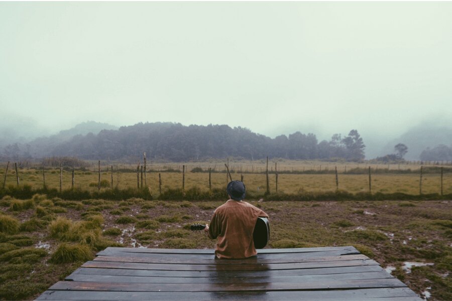 Outdoor in the rain, brown jacket, guitar. Source: https://www.pexels.com/cs-cz/foto/drevo-silnice-rozbresk-krajina-194927/