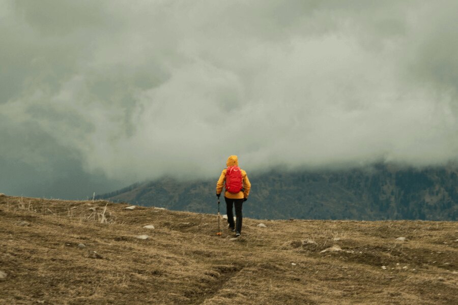 A man in a yellow jacket trekking in the rain in the mountains