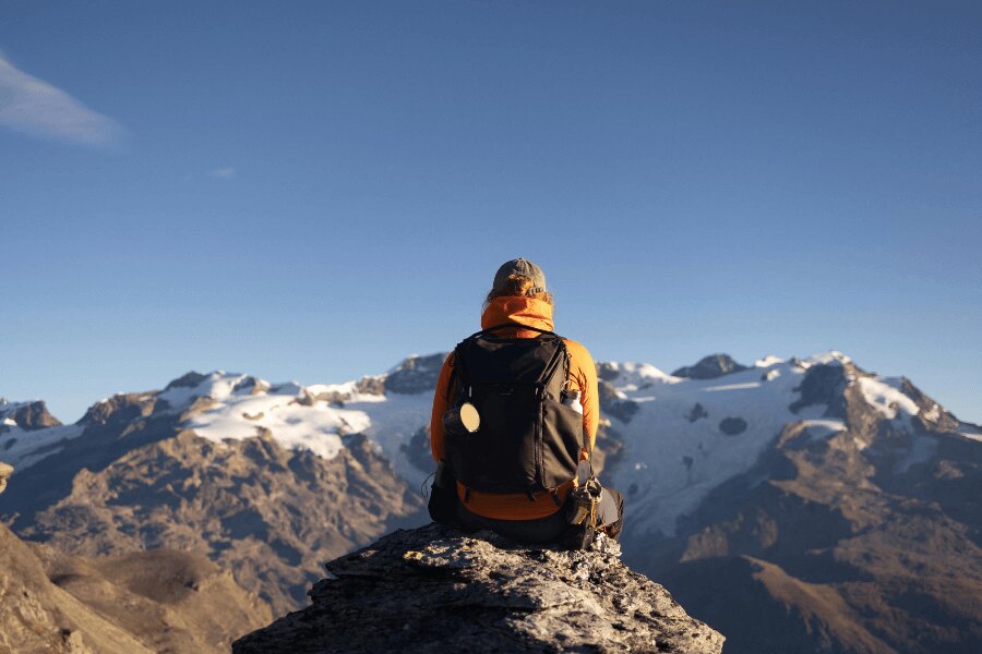 A man in a yellow jacket and a backpack sitting in the mountains. Source: https://www.pexels.com/cs-cz/foto/ryma-studeny-ledovec-snih-20220328/