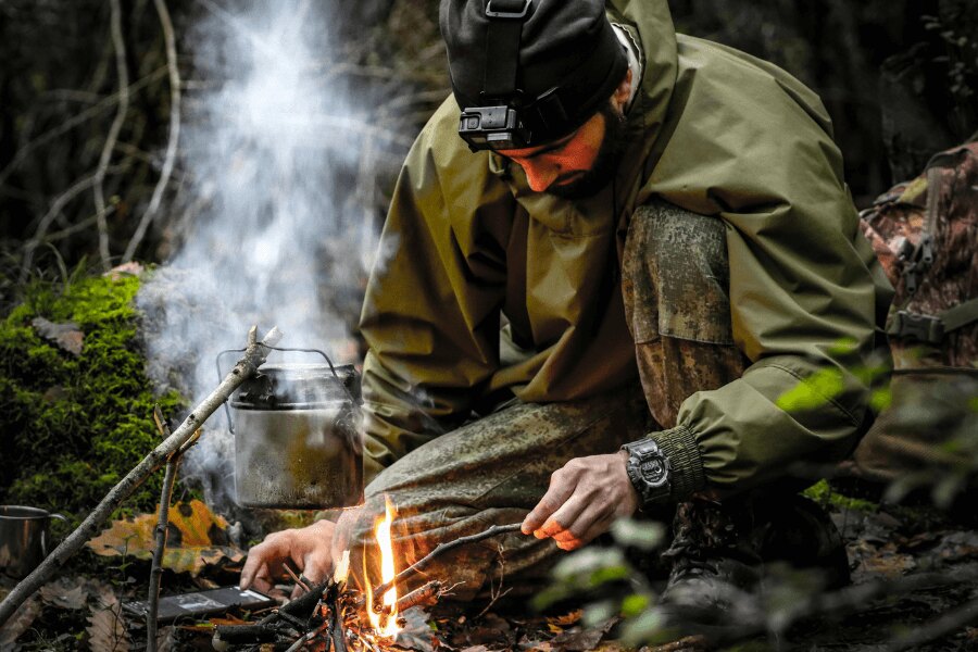 A man in a membrane jacket by fire in the forest. Source: https://www.pexels.com/photo/kneeling-man-starting-fire-in-a-fireplace-15538110/