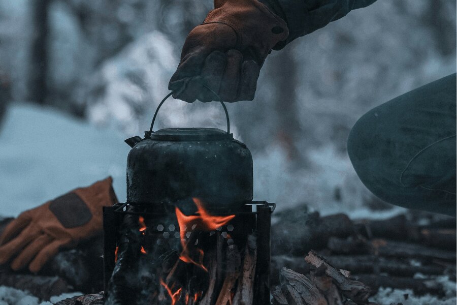 Cooking in an outdoor kettle on a woodstick stove. Source: https://www.pexels.com/cs-cz/foto/ruka-v-rukavici-drzi-konvici-nad-ohnem-v-zime-13611509/