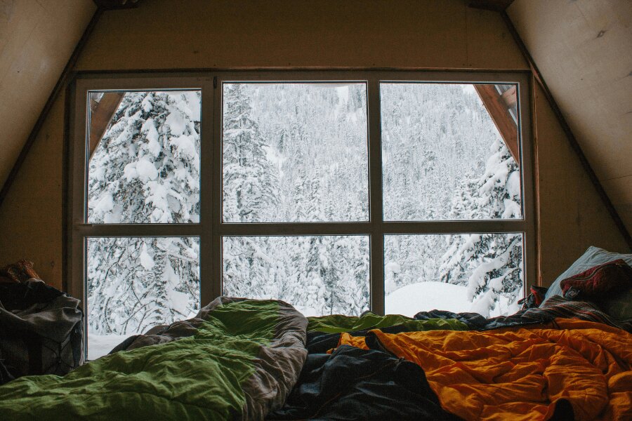 Sleeping bags next to a window in winter mountains in a mountain hut. Source: https://www.pexels.com/cs-cz/foto/ryma-studeny-snih-postel-10346631/